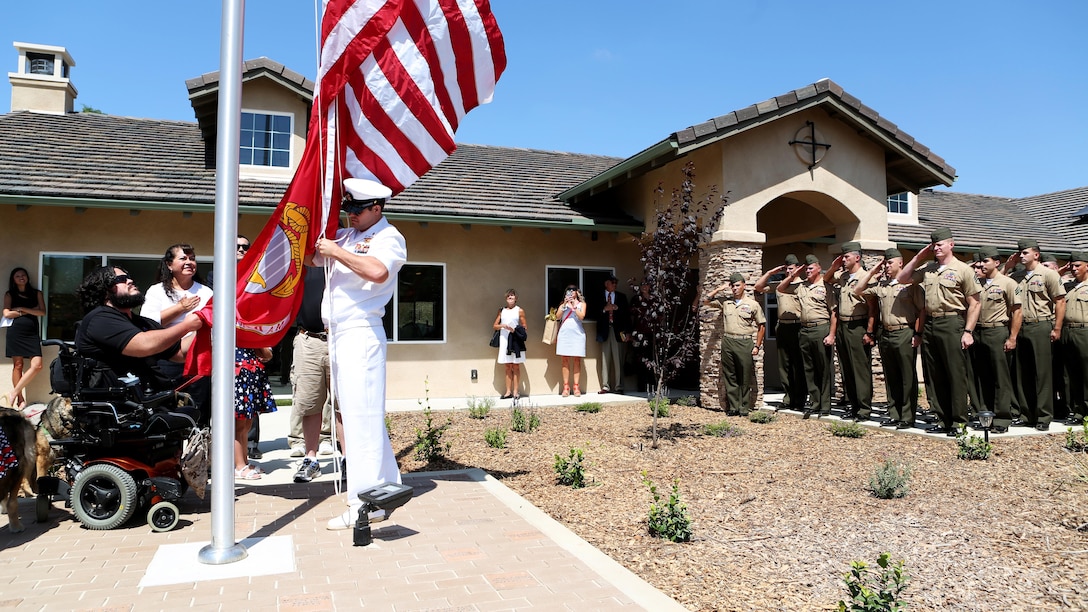 Marines from 1st Explosive Ordnance Disposal Company, 1st Marine Logistics Group look on as retired Staff Sgt. Jason Ross raises the national and Marine Corps colors in front of a new home dedicated to him and his family by The Gary Sinise Foundation in Fallbrook, California, August 221, 2015. Ross was injured by an improvised explosive device in Afghanistan in 2011 while serving as an explosive ordnance disposal technician and lost both of his legs as a result. The new home has smart technology that will significantly reduce the difficulty of everyday tasks for Ross and allow him and his family to live more comfortably.
