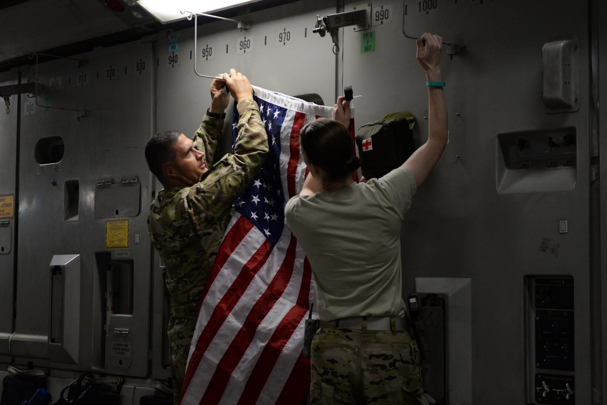 U.S. Air Force Tech. Sgt. Russell “Rusty” McLamb, left, 455th Expeditionary Aeromedical Evacuation Squadron technician deployed from the North Carolina Air National Guard’s 156th Aeromedical Evacuation Squadron, hangs an American flag on a C-17 Globemaster III aircraft on the flight line at Bagram Airfield, Afghanistan, Aug. 8, 2015, prior to an aeromedical evacuation mission to Germany. McLamb is part of the 455th EAES, which is responsible for evacuating the sick and wounded from Central Command to higher echelons of medical care. (U.S. Air Force photo by Maj. Tony Wickman/Released)