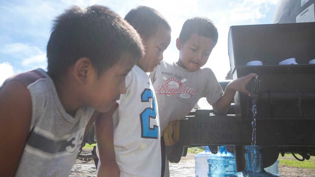 Young boys fill a water jug while U.S. Marines with Combat Logistics Battalion 31, 31st Marine Expeditionary Unit, distribute water to local civilians during typhoon relief efforts in Saipan, Aug. 19, 2015. The Marines with Echo Company, Battalion Landing Team 2nd Battalion, 5th Marines, 31st MEU and CLB 31, 31st MEU, assisted the locals of Saipan by producing and distributing potable water. The Marines and sailors of the 31st MEU were conducting training near the Mariana Islands when they were redirected to Saipan after the island was struck by Typhoon Soudelor Aug. 2-3. 