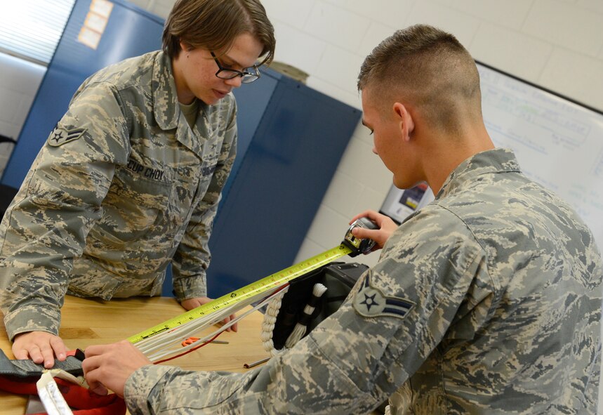 U.S. Air Force Airmen 1st Class Brittany Cup Choy and Kyle Denzine, 20th Operation Support Squadron aircrew flight equipment specialists, measure rope lengths on a parachute at Shaw Air Force Base, S.C., Aug. 24, 2015. This precaution keeps the parachute from becoming unbalanced if a pilot needs to eject from an aircraft. (U.S. Air Force photo by Airman 1st Class Christopher Maldonado/Released)