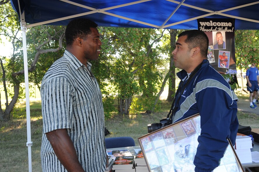 Herschel Walker signs football memorabilia for Staff Sgt. Luis Loza Gutierrez during a meet and greet session Aug. 20, 2015, at the Summer Bash sports grounds on Grand Forks Air Force Base, N.D. Walker spent the day with Airmen and was the guest speaker at the closing ceremony for the day's events. (U.S. Air Force photo/Senior Airman Desiree Economides)
