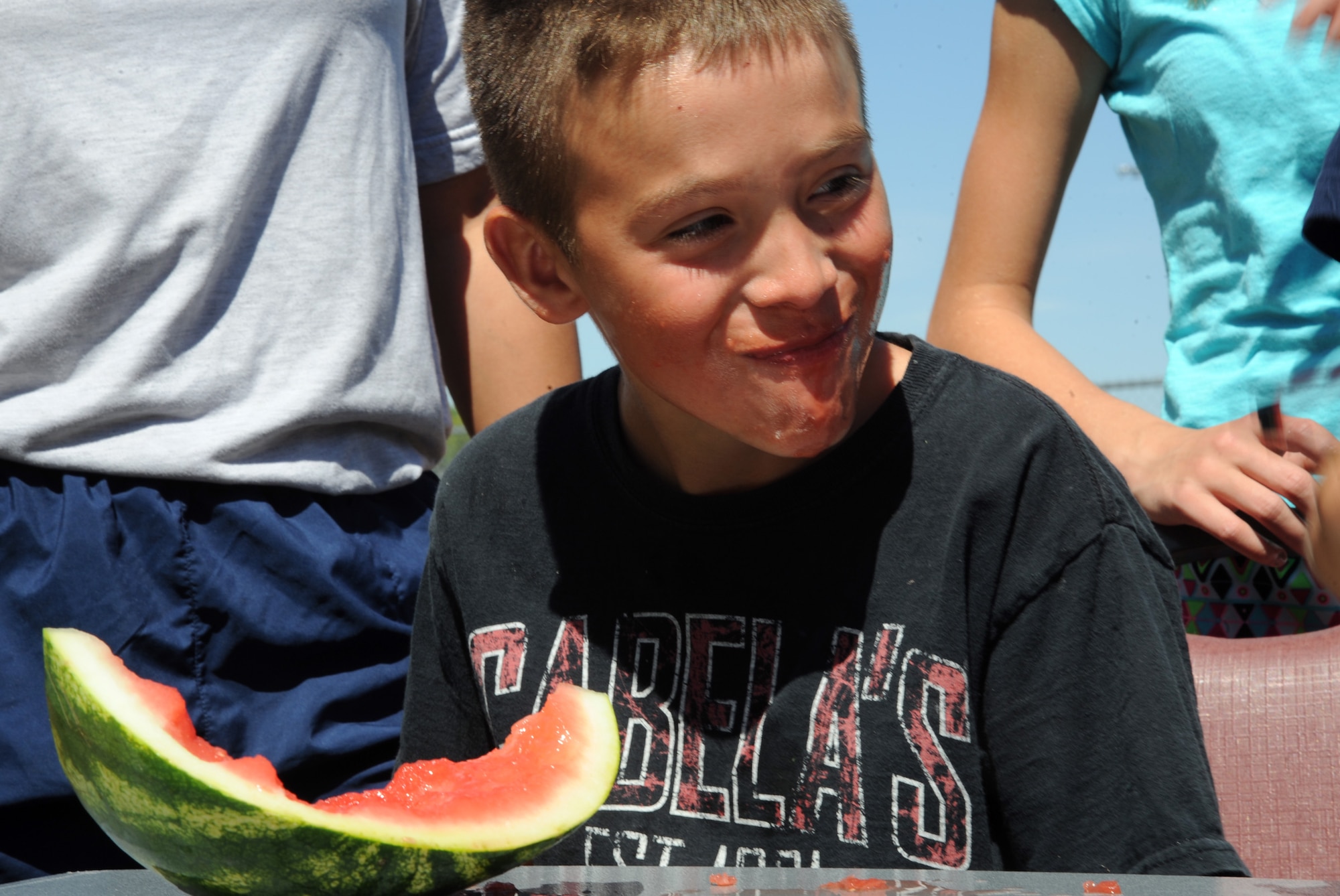 Ten-year-old Jason Cantu smiles while sizing the competition during a watermelon eating contest Aug. 20, 2015, at Grand Forks Air Force Base, North Dakota. The watermelon eating contest was one of many competitions for Airmen and their families to participate in during Summer Bash 2015, an annual morale event at Grand Forks AFB. (U.S. Air Force photo by Senior Airman Desiree Economides/Released)
