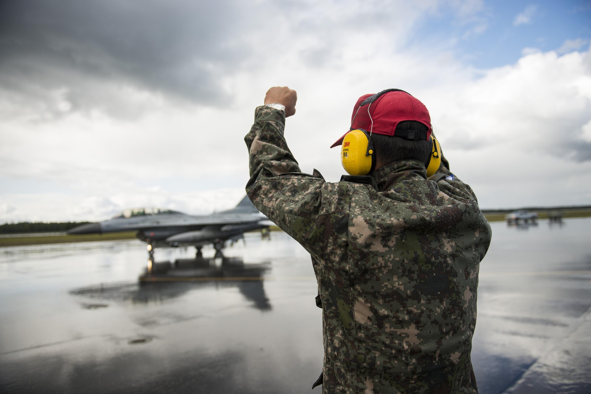Republic of Korea Air Force (ROKAF) Warrant Officer Dongjun Lee, a ROKAF maintenance officer, signals to the pilots of a ROKAF F-16D Fighting Falcon after marshaling the aircraft through an unexpected rainstorm for a RED FLAG-Alaska (RF-A) 15-3 sortie, Aug. 11, 2015 at Eielson Air Force Base, Alaska. RF-A sorties are conducted for the full two-weeks, rain or shine, barring extreme inclement weather, providing participants with unparalleled training in the world’s largest instrumented air, ground and electronic combat training range in the world, the Joint Pacific Alaska Range Complex. (U.S. Air Force photo by 1st Lt. Elias Zani/Released)