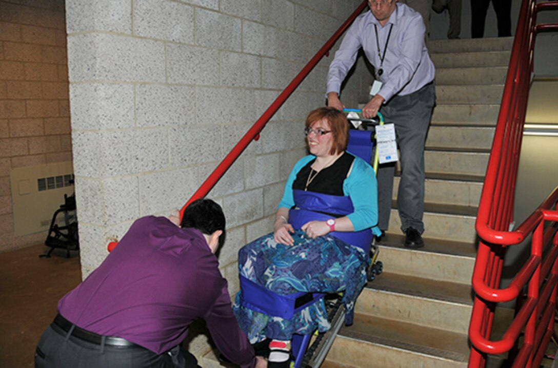 Vivian d’Alelio, a management assistant with DLA Headquarters’ Multimedia Division, is lowered down a flight of stairs in a safety chair by McNamara Headquarters Complex employees during a simulated emergency evacuation April 29. The training was designed to help employees with mobility challenges descend stairwells and develop strategies to assist them during an emergency.