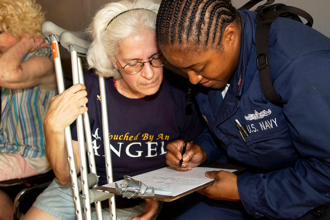 A sailor helps a Hurricane Katrina victim fill out paperwork after she was transported to the dock landing ship USS Tortuga in New Orleans, Sept. 5, 2005. Docked in the city, the Tortuga provided hot meals, showers and beds for the victims.  U.S. Navy photo by Petty Officer 2nd Class Michael B. Watkins 