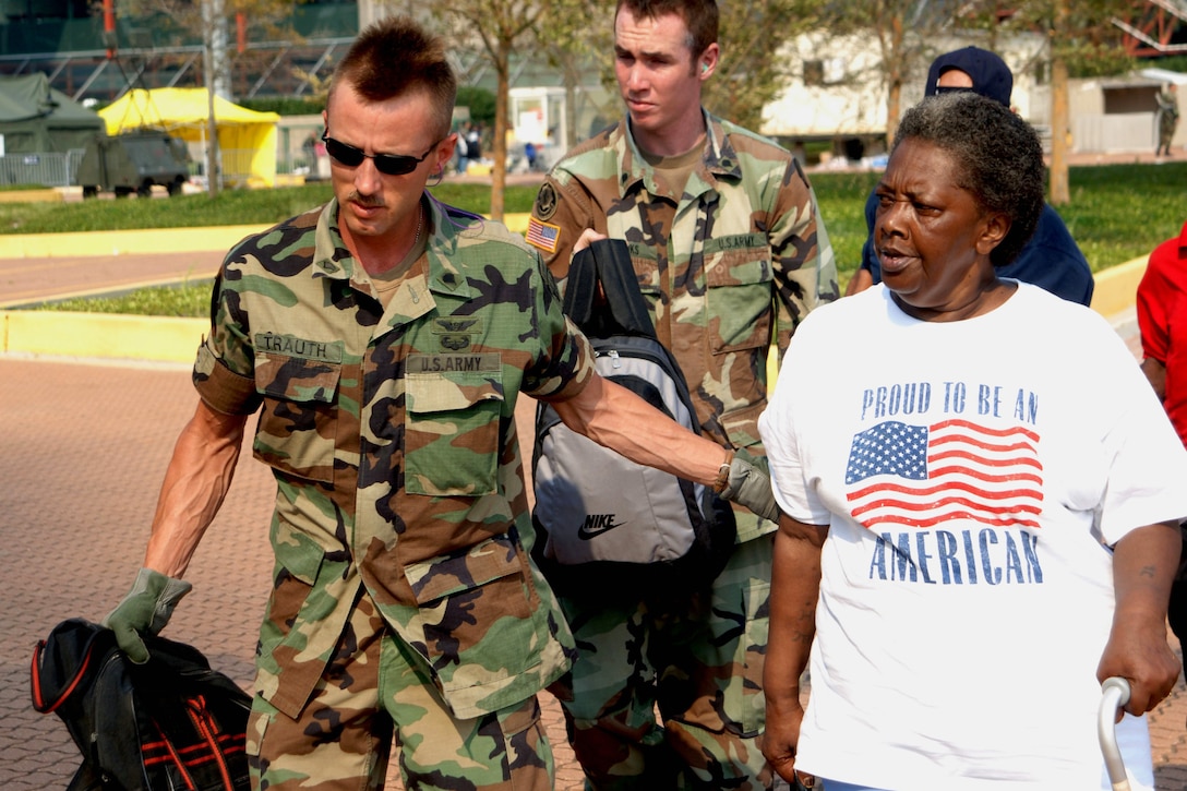 Army Spcs. Trauth and Hanks, members of the Army National Guard, escort hurricane victims to a Army CH-47 Chinook helicopter during Hurricane Katrina relief efforts in New Orleans, La., Sept. 3, 2005. The guardsmen participated in humanitarian assistance operations, a joint effort led by the Defense Department of Defense and the Federal Emergency Management Agency. U.S. Navy photo by Petty Officer 1st Class  Robert McRill