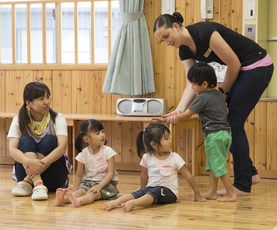 Pfc. Makayla Whitney, a postal clerk with Headquarters and Headquarters Squadron based aboard Marine Corps Air Station Iwakuni, Japan, shows students at Josho Hoikuen School in Iwakuni City, how to play duck, duck, goose during a community relations event hosted by the Marine Memorial Chapel, Aug. 11, 2015. Service members commit to building positive relationships with the local community by participating in these events.