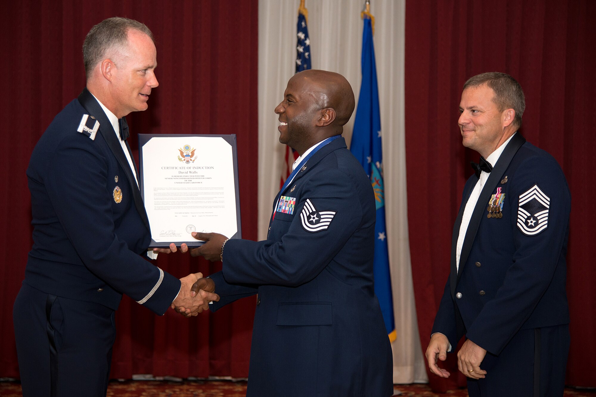 Col. Michael A. Vogel, 66th Air Base Group commander, presents a certificate to Tech Sgt. David Walls, Joint Personal Property Shipping Office-Northeast storage management NCO in charge, during the Senior NCO Induction Ceremony at the Minuteman Commons Aug. 20, while Chief Master Sgt. David Anthony, the event's guest speaker, looks on. Eleven Airmen were inducted into the senior NCO corps during the ceremony. (U.S. Air Force photo by Mark Herlihy)