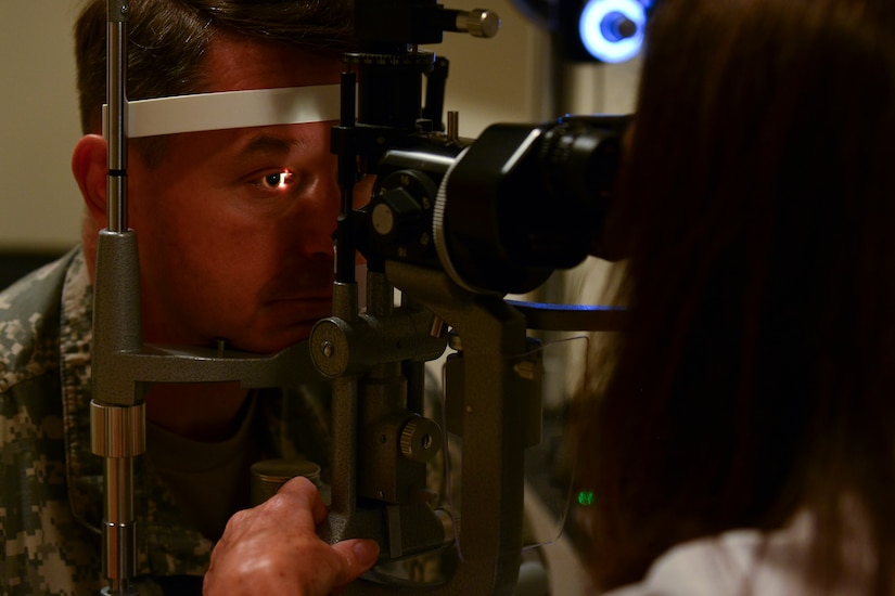 Dr. Robin Collard, McDonald Army Health Center Eye Clinic optometrist, looks through a slit lamp during an eye exam at Fort Eustis, Va.  Aug. 21, 2015. The lamp allowed her to view the eye structures of U.S. Army Col. Glenn Hodges’, U.S. Army Training and Doctrine Command Army Capabilities Integration Center human performance and learning analyst. (U.S. Air Force photo by Staff Sgt. Natasha Stannard/Released)