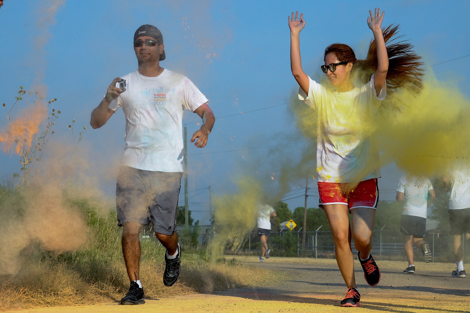 U.S. Air Force Capt. Jason R. Crosby, 17th Training Wing executive officer, and Patricia Crosby run through a plum of color powder during the Sexual Assault Prevention and Response 5K Color Race at Kiowa Trail on Goodfellow Air Force Base, Texas, Aug. 22. 2015. Volunteers threw varying colors of powder on participants during the course of the race. (U.S. Air Force photo by Airman Caelynn Ferguson/Released)