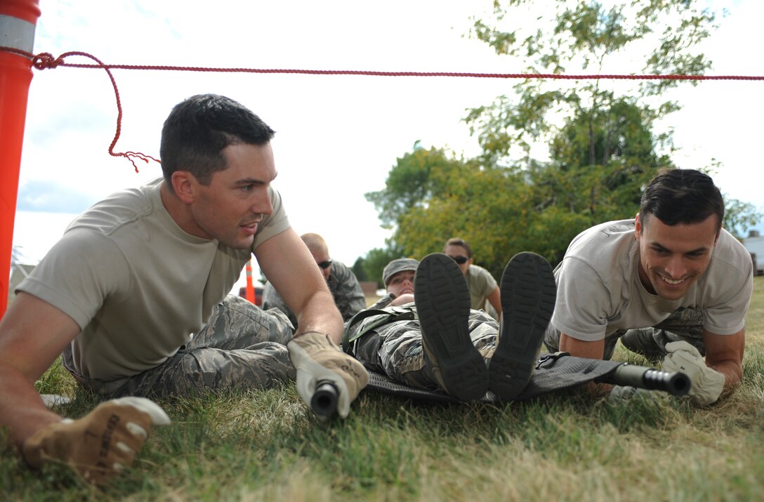 Capt. Brandon Kvidt (left), 28th Medical Group clinical dentist, and Capt. Timothy Aylward (right), 28th MDG physician assistant, low crawl while moving a simulated patient toward the finish line of a litter obstacle at Ellsworth Air Force Base, S.D., Aug. 19, 2015. The event was part of a field training exercise that consisted of four stations: Alaskan shelter-setup, ambulance loading, litter carrying and self-aid buddy care. (U.S. Air Force photo by Airman Sadie Colbert/Released)