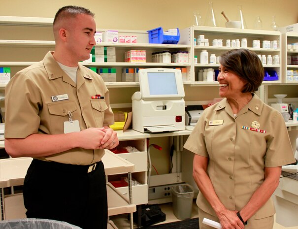 Hospitalman Dalton Terrell, pharmacy technician, Naval Health Clinic Charleston, describes the daily operations of and services provided at NHCC's pharmacy, for Rear Adm. Raquel Bono, chief, Navy Medical Corps and director, National Capital Region Medical Directorate , Aug. 21, 2015 during Bono's visit to NHCC. Bono also met with NHCC command leadership, visited various departments throughout the clinic, and spoke with staff members about the future of Navy medicine and what's on the horizon for military health care through the collaboration of joint service operations. (Navy photo/ Hospitalman Mark Simon)