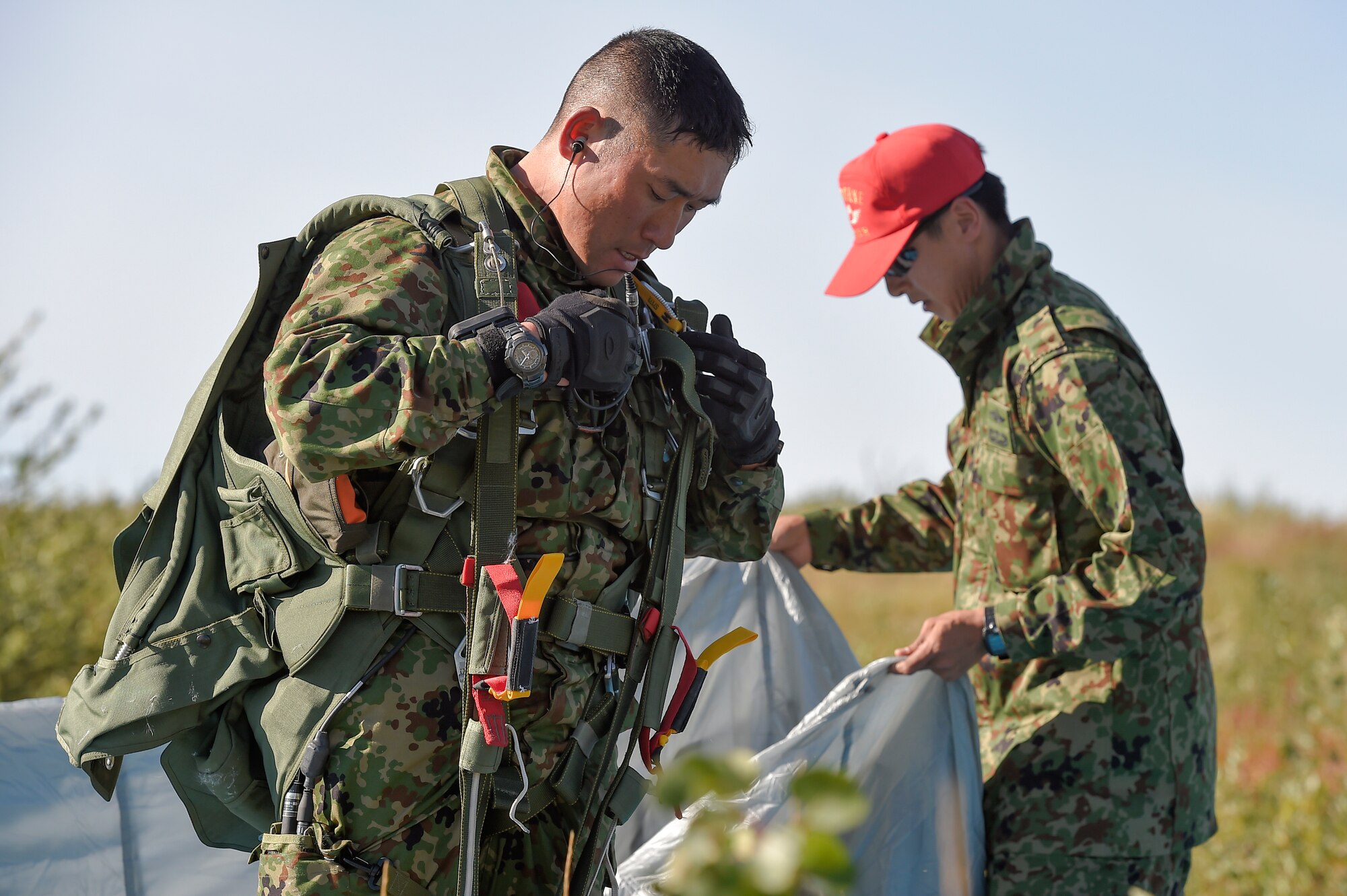 Japanese Ground Self-Defense Force Sgt. Kuniaki Iwakura, left, from Chiba prefecture, removes his parachute rigging after conducting a practice high altitude-low opening jump on Malemute drop zone, Joint Base Elmendorf-Richardson, Alaska, Aug. 24, 2015. JGSDF and U.S. Army paratroopers conducted the practice jump utilizing Royal Australian and U.S. Air Force aircraft as part of Pacific Airlift Rally 2015, a biennial, multilateral tactical military symposium designed to enhance military airlift interoperability and cooperation between nations of the Pacific region for future humanitarian missions. (U.S. Air Force photo/Alejandro Pena)