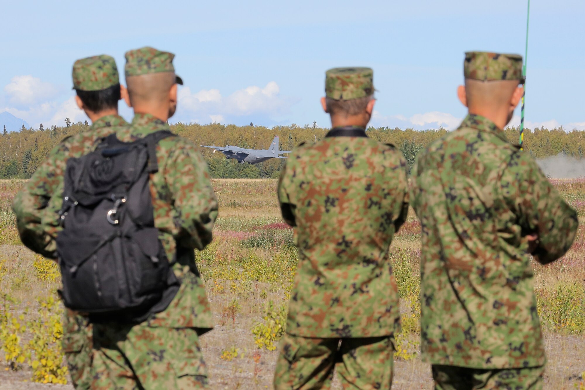 Japanese Ground Self-Defense Force soldiers watches a U.S. Air Force C-130 Hercules, assigned to the 374th Wing from Yokota Air Base, take off from Malemute drop zone, Joint Base Elmendorf-Richardson, Alaska, Aug. 24, 2015. JGSDF and U.S. Army paratroopers conducted the practice jump utilizing Royal Australian and U.S. Air Force aircraft as part of Pacific Airlift Rally 2015, a biennial, multilateral tactical military symposium designed to enhance military airlift interoperability and cooperation between nations of the Pacific region for future humanitarian missions. (U.S. Air Force photo/Alejandro Pena)