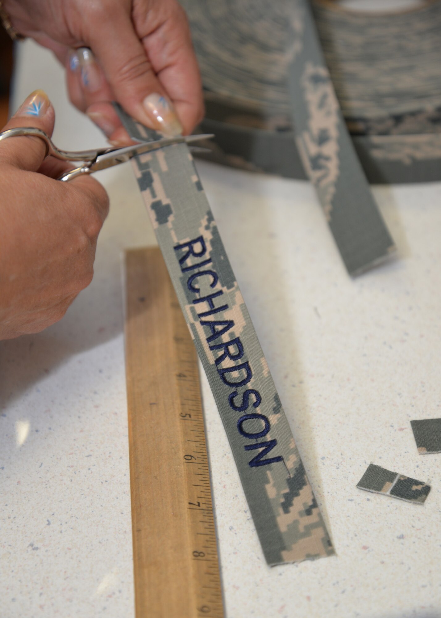 Sarah Jakes, 100th Force Support Squadron Arts and Crafts embroiderer from Mildenhall, Suffolk, finishes name tapes for a customer Aug. 20, 2015, on RAF Mildenhall, England. Additionally, Jakes embroiders clothing, baseball caps and other similar items. The 100th FSS facility can frame photos and other items for customers, engrave onto products made of materials such as glass, wood and slate, and create unique items for leaving gifts or awards. (U.S. Air Force photo by Karen Abeyasekere/Released)