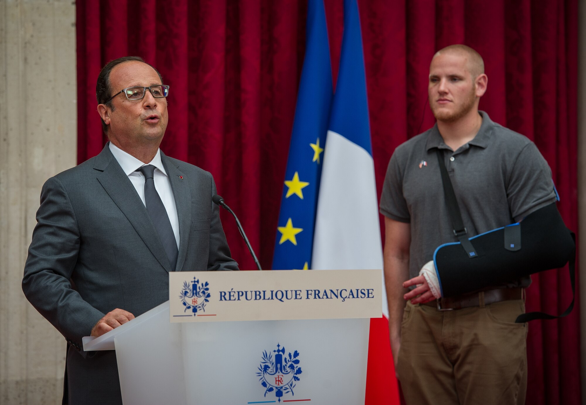 U.S. Airman 1st Class Spencer Stone looks on as French President Fran??ois Hollande speaks to a crowd of dignitaries during a Legion of Honor ceremony at his home in Paris Aug. 24, 2015, following a foiled attack on a French train. Stone was on vacation with his childhood friends, Aleksander Skarlatos and Anthony Sadler, when an armed gunman entered their train carrying an assault rifle, a handgun and a box cutter. The three friends, with the help of a British passenger, subdued the gunman after his rifle jammed. Stone???s medical training prepared him to begin treating wounded passengers while waiting for the authorities to arrive. Stone is an ambulatnce service technician with the 65th Medical Operations Squadron stationed at Lajes Field, Azores. (U.S. Air Force photo/Tech. Sgt. Ryan Crane)