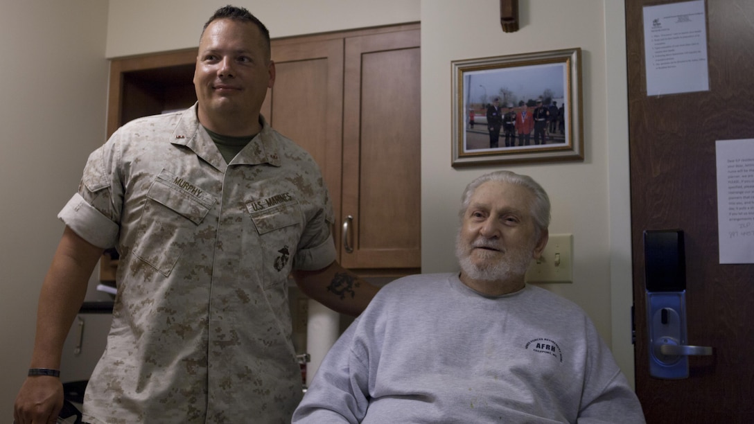 CWO 4 Jerod Murphy, assistant ordnance officer for 1st Marine Division, and John Morash Sr., a retired Marine, pose together at the Armed Forces Retirement Home in Gulfport, Miss., August 12, 2015. Murphy visited the home regularly to eat meals with Morash and other veterans when he was stationed in Gulfport in 2005. Murphy assisted with evacuating injured residents of the home during Hurricane Katrina and transporting them to the hospital.