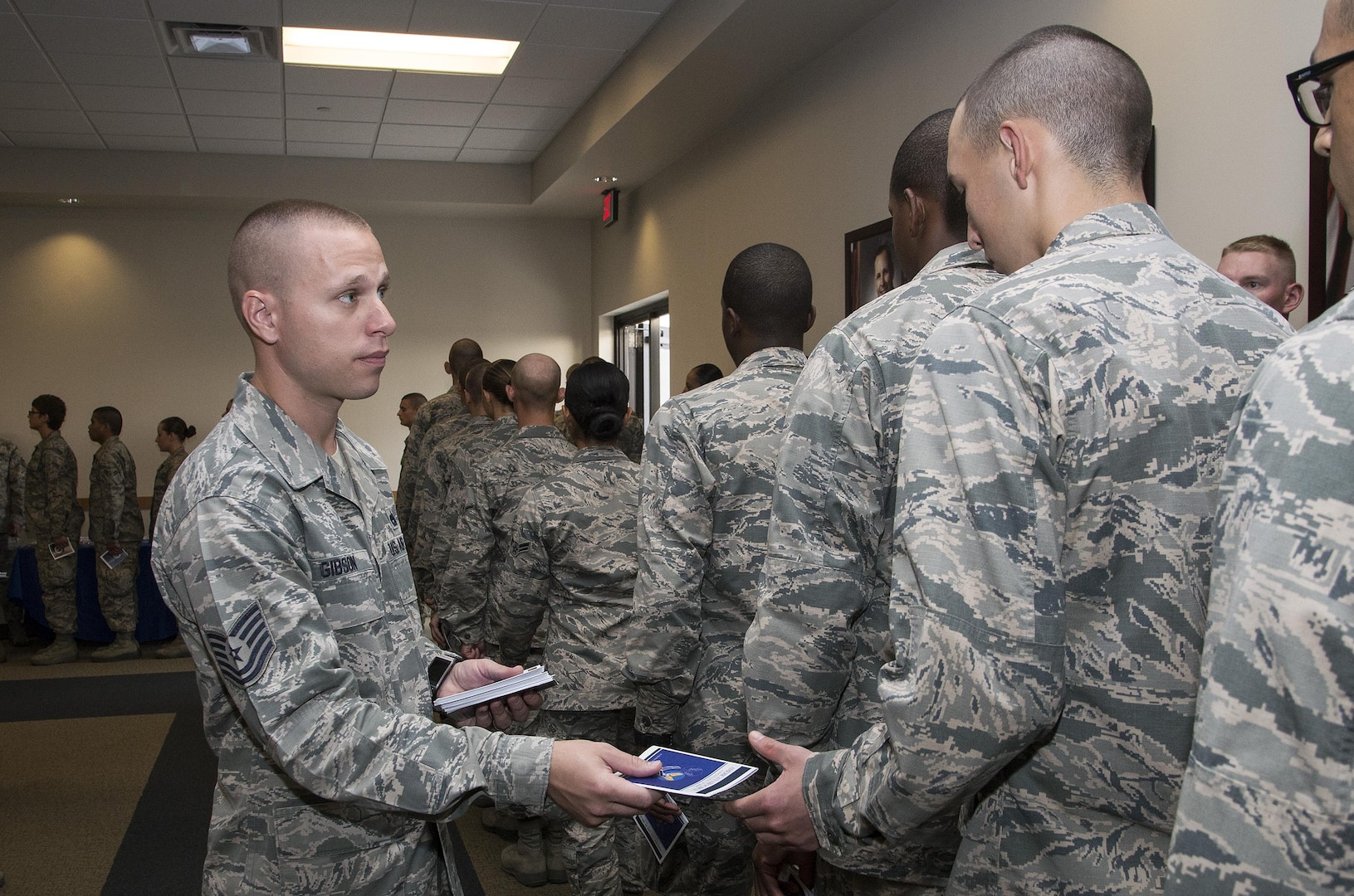 Tech. Sgt. Michael Gibson, 326th Training Squadron military training instructor, passes out Little Blue Books to Airmen during a visit from Secretary of the Air Force Deborah Lee James, Air Force Chief of Staff General Mark A. Welsh III and Chief Master Sergeant of the Air Force James A. Cody to Joint Base San Antonio-Lackland, Texas Aug. 27, 2015. The Airmen received a copy of "America's Air Force: A Profession of Arms," the next evolution of the "Little Blue Book" previously released in 1997. The new book gives Airmen instant access to the core values, codes and creeds that guide Airmen as they serve in the Profession of Arms. The book will be distributed to all new Airmen before transitioning to technical training and available online through Air Force e-publishing. 