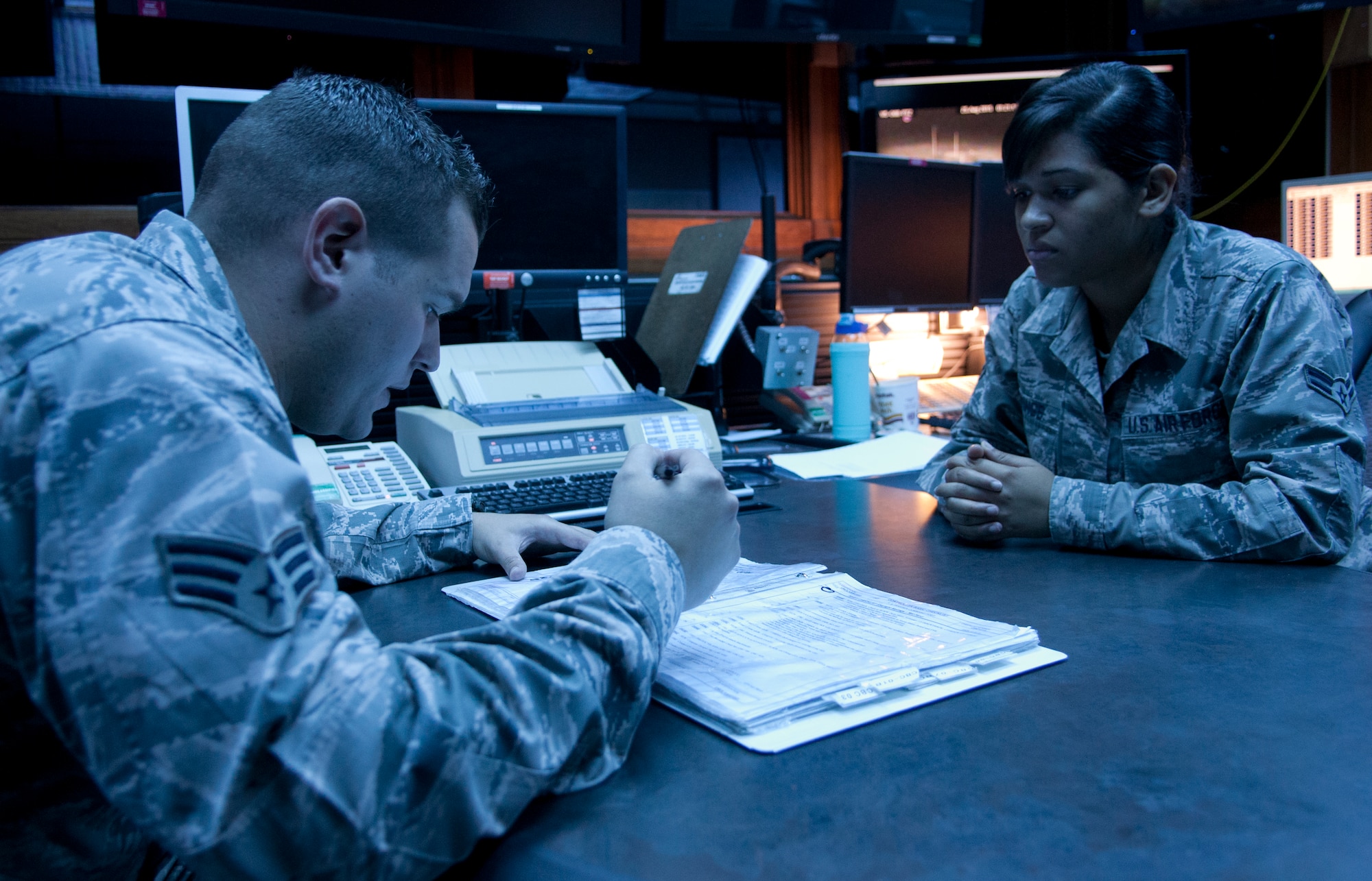 Senior Airman Zachary Pirrung, 90th MW Command Post senior emergency action controller, goes over the daily checklist with Airman 1st Class Chanel Cummings, his junior emergency action controller at 1:21 a.m., Aug. 25, 2015, in the command post. The lights in the secured area are tinted blue to calm the crew members and limit glare on checklists and other documents used in the facility. (U.S. Air Force photo by Airman 1st Class Malcolm Mayfield)