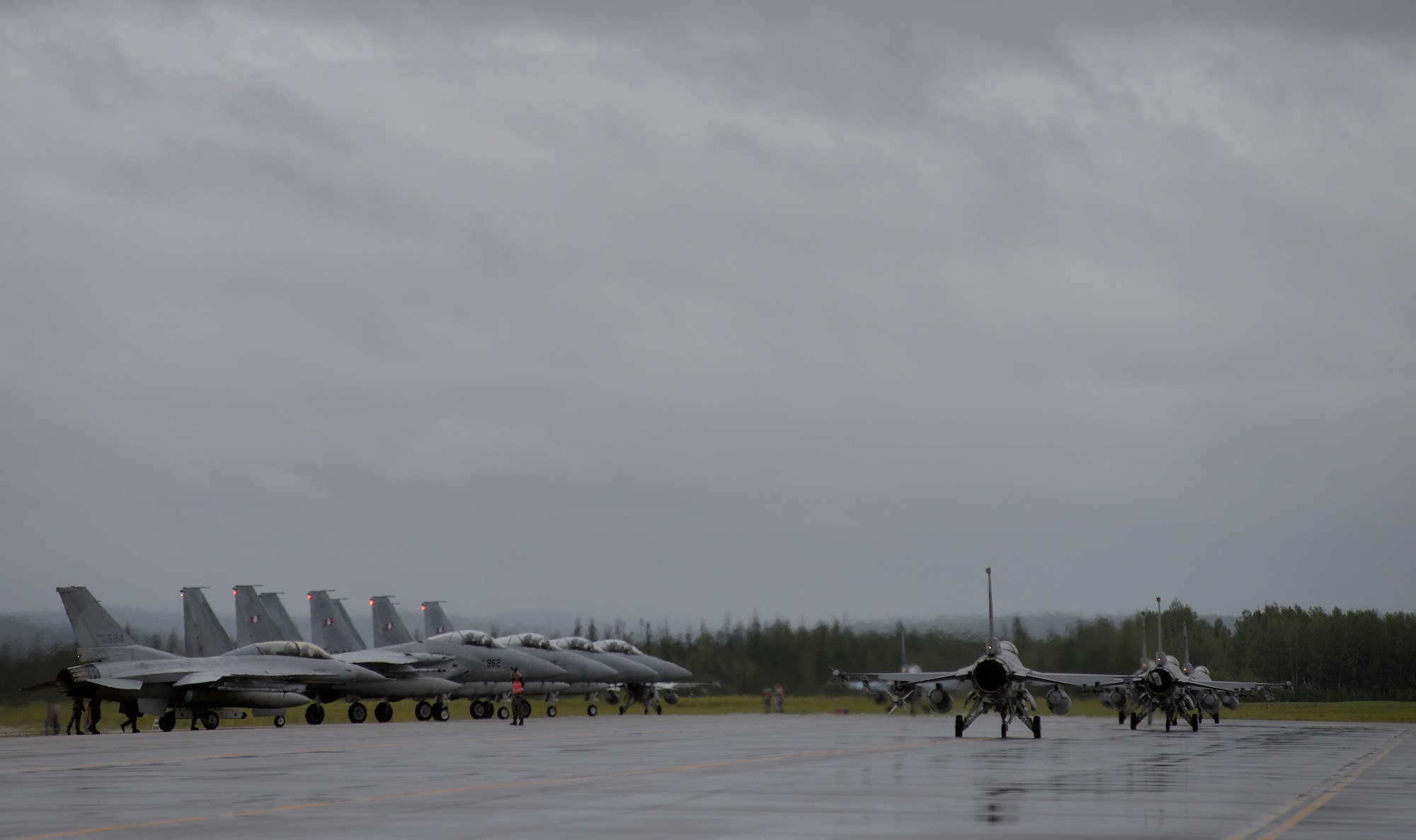A Republic of Korea Air Force (ROKAF) crew chief marshals in ROKAF F-16 Fighting Falcons alongside Japan Air Self-Defense Force F-15J Eagles at the end of the Eielson Air Force Base, Alaska, flightline Aug. 10, 2015, as U.S. Air Force F-16s taxis out to the runway for the first simulated combat sortie launch of RED FLAG-Alaska (RF-A) 15-3. Various units from in and outside the Pacific Air Forces (PACAF) area of operations as well as sister service and partner nation units are deployed to Eielson for RF-A, a series of PACAF commander-directed field training exercises for U.S. and partner nation forces, providing combined offensive counter-air, interdiction, close air support, and large force employment training in a simulated combat environment. (U.S. Air Force photo by Master Sgt. Karen J. Tomasik/Released)
