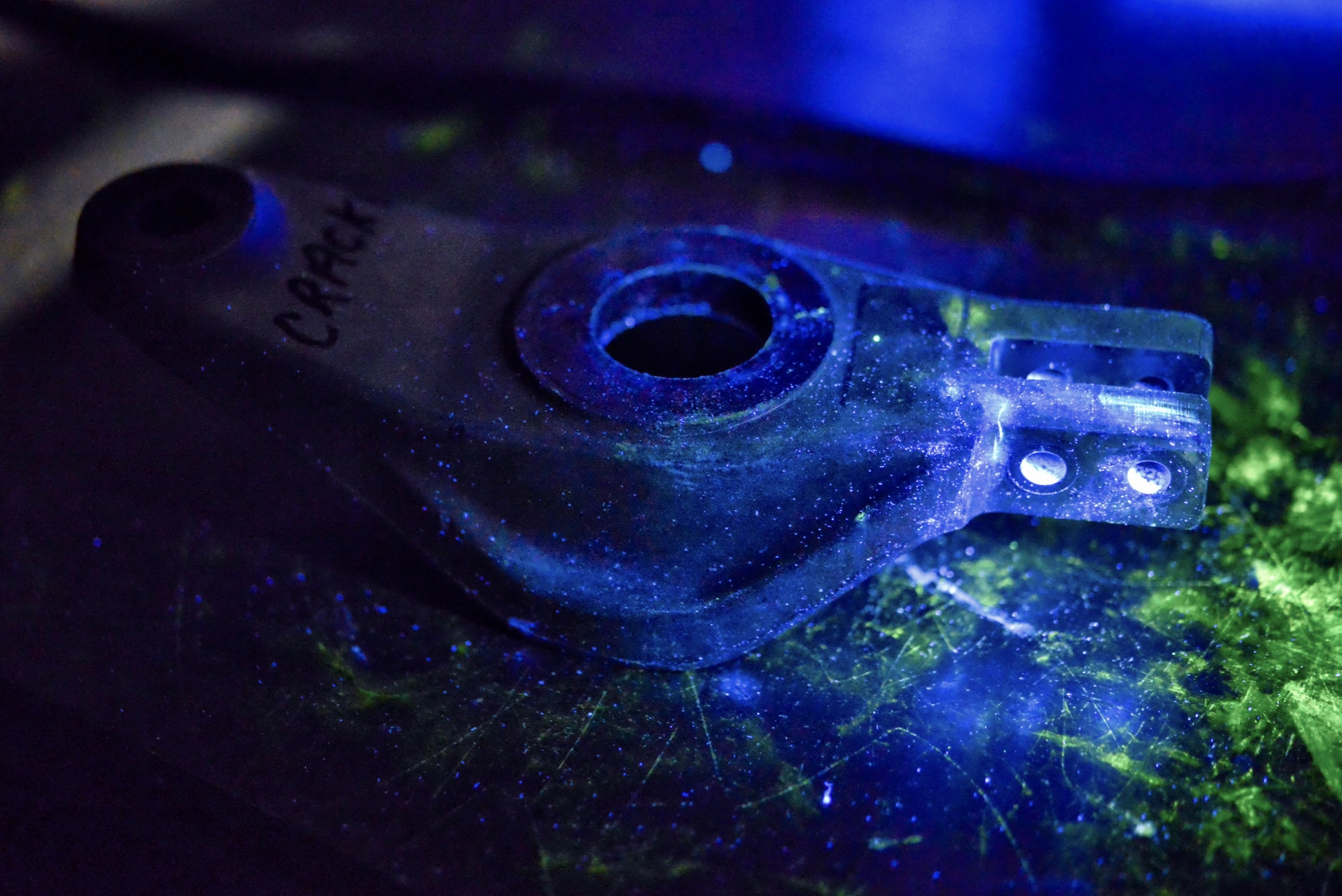 A piece of metal used for training sits under a black light during a fluorescent penetrant inspection, Aug. 25, 2015, at Yokota Air Base, Japan. Nondestructive inspection technicians train with fluorescent light, enabling them to view cracks that are not visible to the human eye. (U.S. Air Force photo by Airman 1st Class Delano Scott/Released)