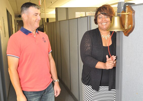 Project manager Matthew Morelan watches as contract specialist Jennifer Letson rings a bell after the Utility Monitoring and Control Systems program team awarded the first of the last 75 task orders for the fiscal year. To help build morale, the UMCS team bell will ring after each task order is awarded.