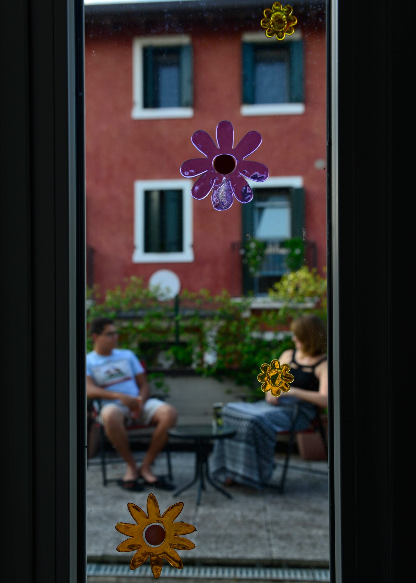 Gel flowers stick on the window as U.S. Air Force Airman Matthew Medina, 31st Aircraft Maintenance Squadron weapons load member, and his wife, Alexis, talk on their back patio at their new home, Aug. 28, 2015, near Aviano Air Base, Italy. Alexis placed the flowers as her first addition to the couple’s home when she arrived. (U.S. Air Force photo by Airman 1st Class Cary Smith/Released)
