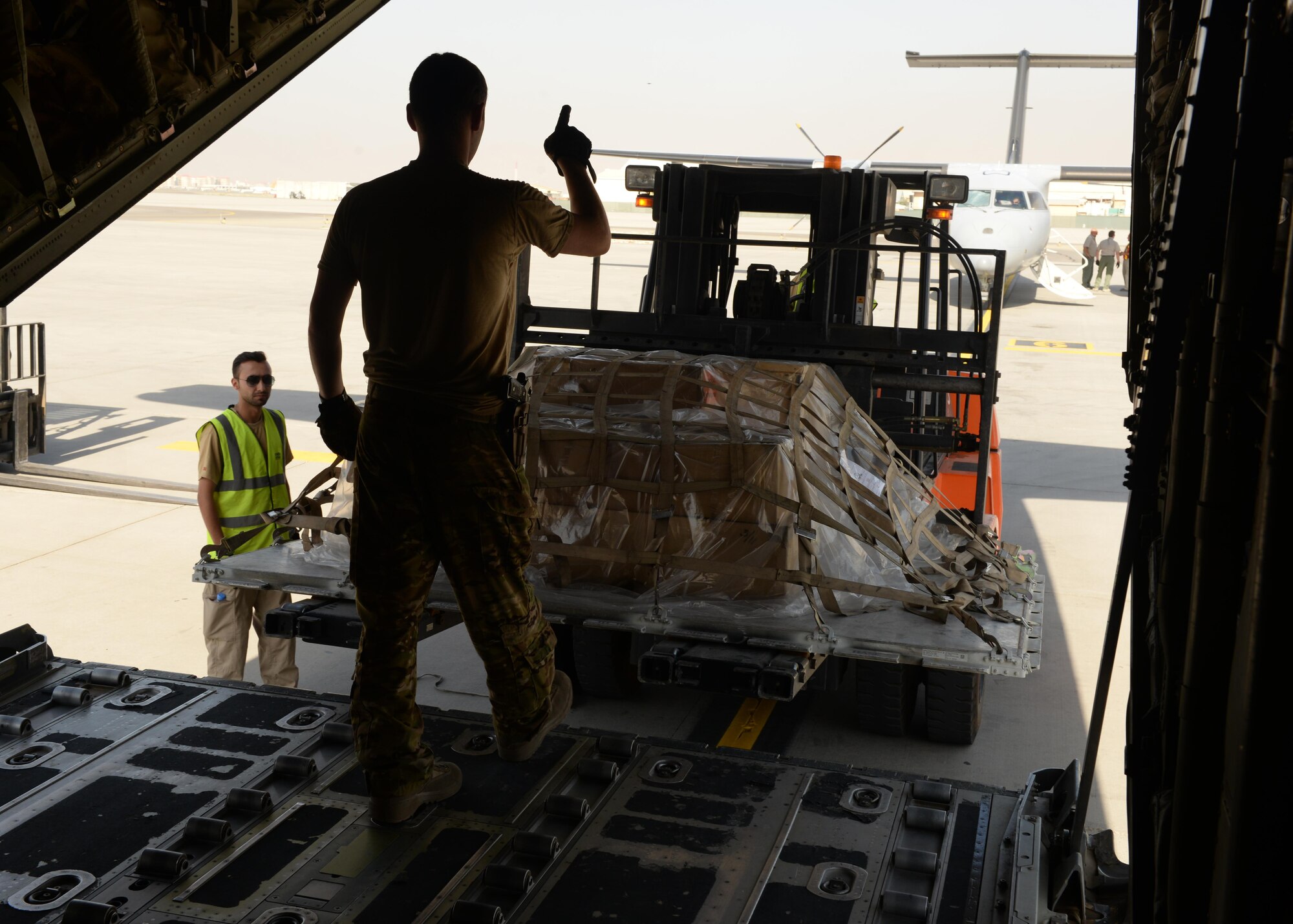 U.S. Air Force Staff Sgt. Casey Strauss, 774th Expeditionary Airlift Squadron C-130J Super Hercules aircraft loadmaster, gives directions to a cargo loader during a shipment pick-up Aug. 28, 2015, at Hamid Karzai International Airport in Kabul, Afghanistan. Strauss and his fellow loadmasters are responsible for loading and unloading cargo, passenger safety in flight, and ensuring the aircraft stays within the proper weight and balance limitations. (U.S. Air Force photo by Senior Airman Cierra Presentado/Released)
