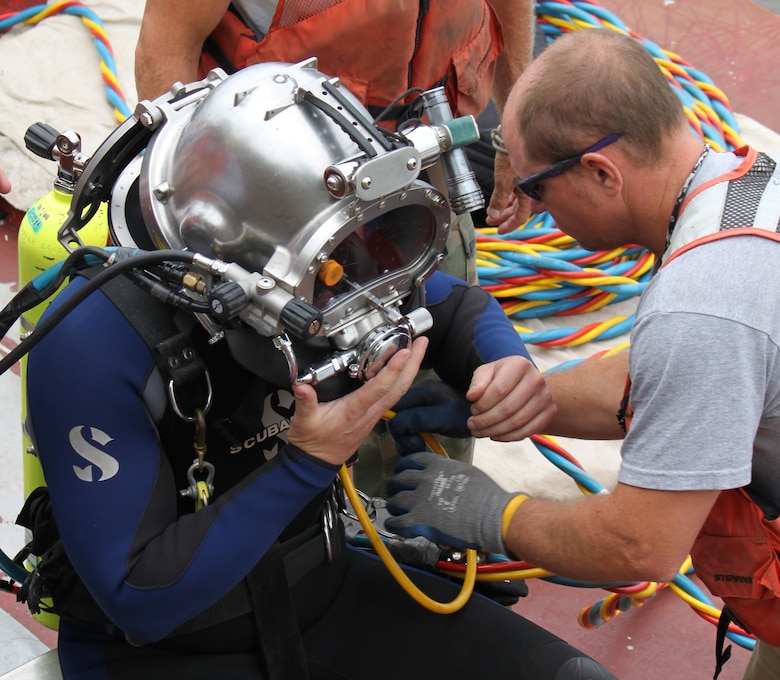 District dive team member, Mark Hoewing (right),shifthead at Lock and Dam 20,helps Nathan Gorham, assistant lockmaster at Locks and Dam 15, with securing his dive helmet in preparation for a dive at Locks and Dam 15.