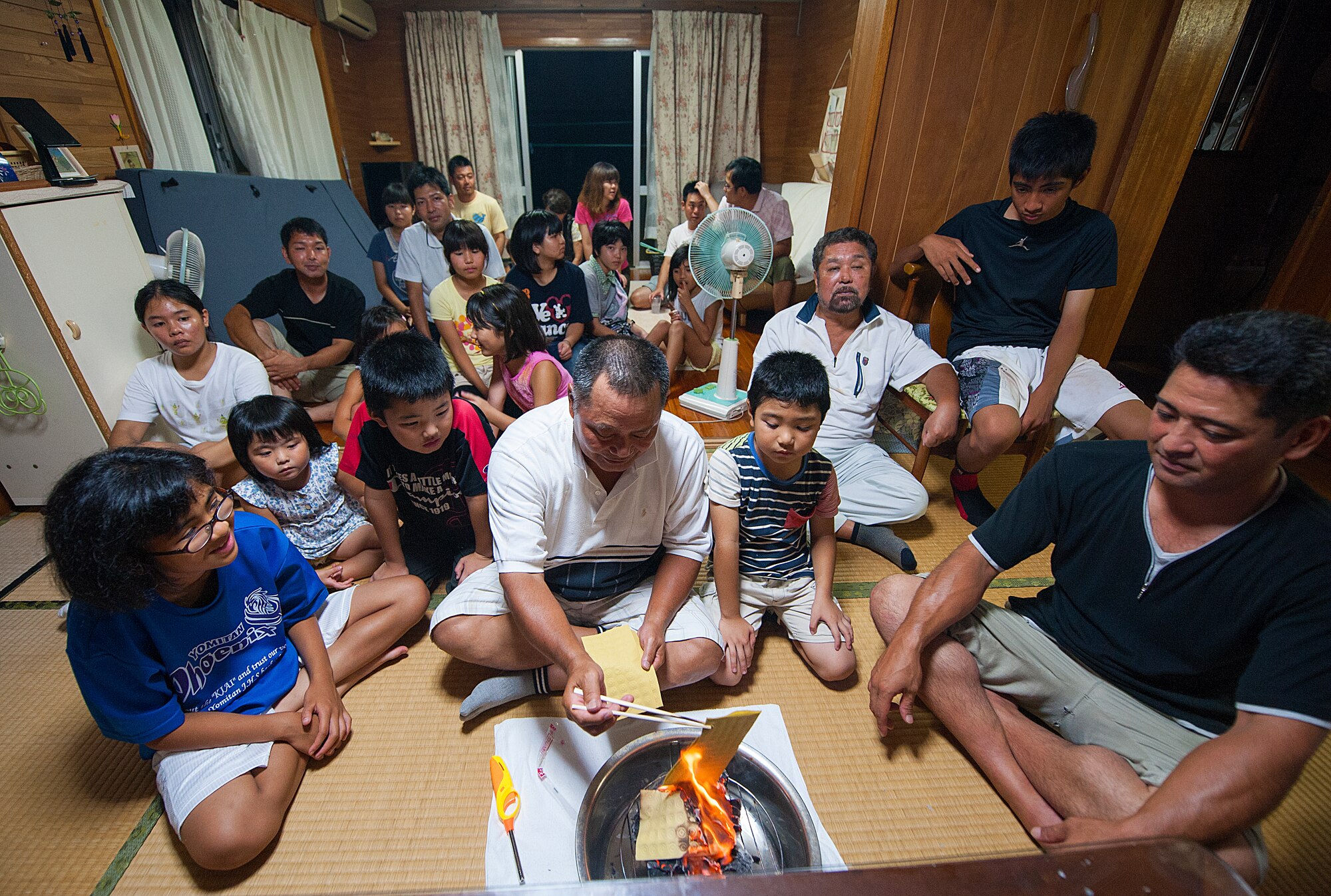 Sousei Yamakawa, owner of the house, burns uchikabi, money of the other world, while surrounded by relatives in Yomitan village, Okinawa, Japan, Aug. 28, 2015. Okinawans invite their ancestral spirits to visit the family's Buddhist altar during this traditional period. (U.S. Air Force photo by Naoto Anazawa)