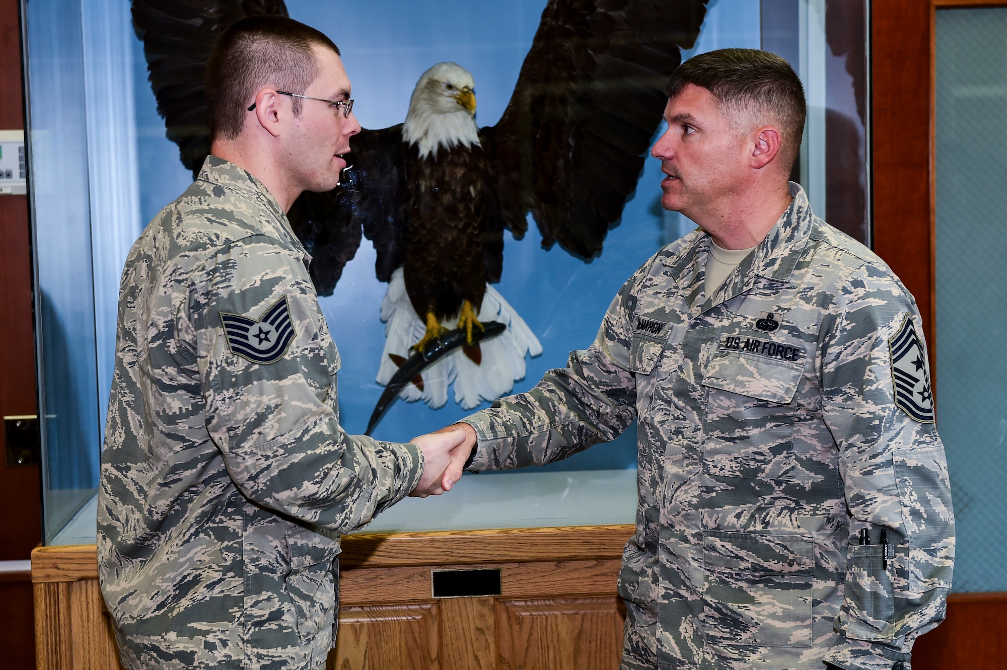 Tech. Sgt. Nicholas Rau, 460th Space Wing Public Affairs NCOIC of community engagement, left, receives a coin from Chief Master Sgt. Patrick McMahon, Air Force Space Command command chief, Aug. 28, 2015, at the 460th SW Headquarters Building on Buckley Air Force Base, Colo. McMahon visited Buckley AFB for the first time after becoming the senior enlisted leader of Air Force Space Command, communicating his goals, answering Airman’s questions and recognizing outstanding performers. (U.S. Air Force photo by Senior Airman Phillip Houk/Released)