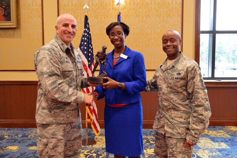 Col. Kenneth Moss, 43rd Airlift Group commander, left, and Chief master Sgt. Kenneth Hubbard, 43rd Air Mobility Squadron superintendent, right, present an Iron Mike trophy to Kady-Ann Davy, Fayetteville mayor pro tem, in appreciation for her attendance and speech at the Women’s Equality Day observance Aug. 26, 2015, held at the Catering and Conference Center, Fort Bragg, North Carolina. (U.S. Air Force photo/Marvin Krause)