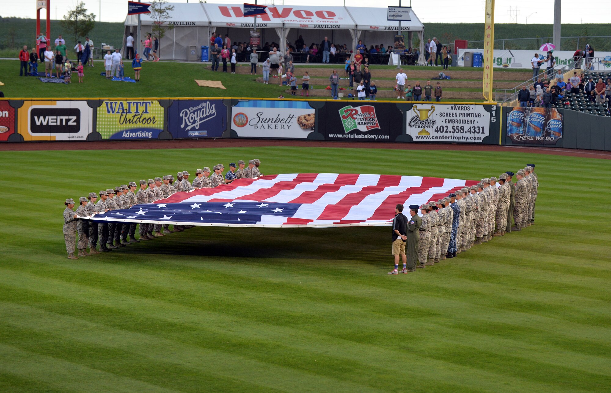 Members of the U.S. armed services unfurl a large American Flag in Werner Park’s center field as part of military appreciation night on Aug. 28, Papillion, Nebraska.  Werner Park, home of the Storm Chasers baseball team, is located 10 miles from the gates of Offutt Air Force Base.  (U.S. Air Force photo by Josh Plueger/Released)
