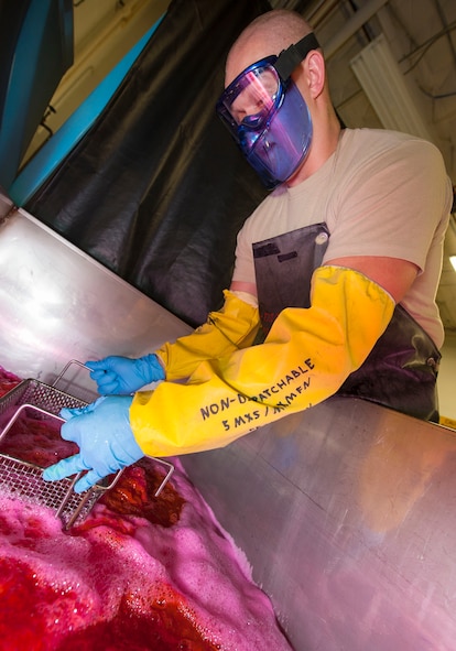 Senior Airman Kyle Abendroth, 5th Maintenance Squadron non-destructive inspection journeyman, dips a basket into remover at Minot Air Force Base, N.D., Aug. 26, 2015. The remover bath is the third step in chemically identifying pits, cracks and other damage that is invisible to the naked eye. (U.S. Air Force photo/Senior Airman Stephanie Morris)