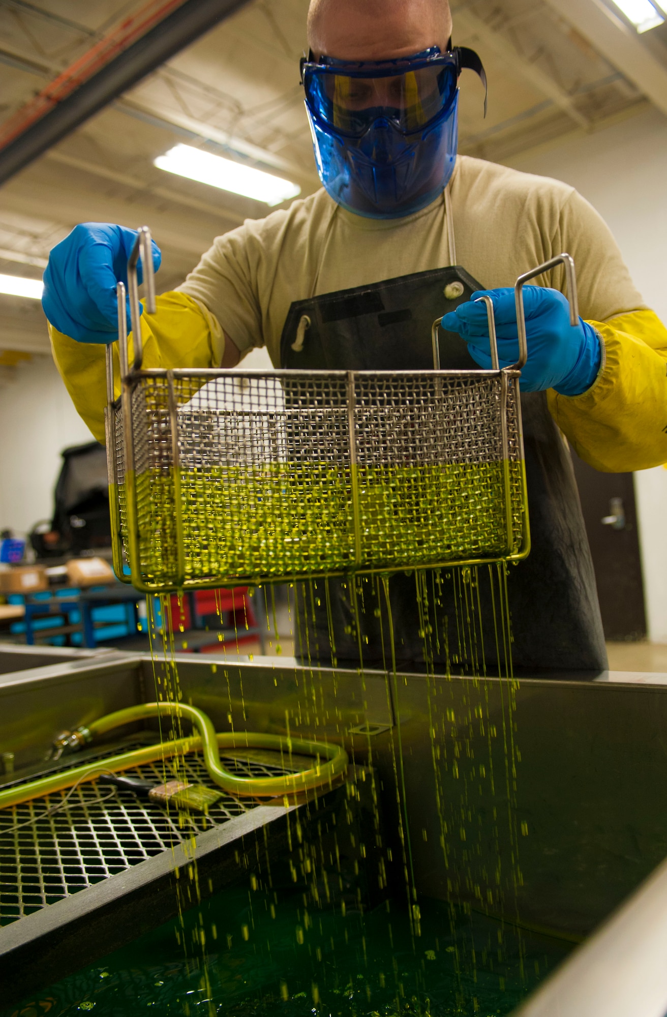 Senior Airman Kyle Abendroth, 5th Maintenance Squadron non-destructive inspection journeyman, dips a basket into penetrant at Minot Air Force Base, N.D., Aug. 26, 2015. The penetrant bath is the first step in chemically identifying pits, cracks and other damage that is invisible to the naked eye. (U.S. Air Force photo/Senior Airman Stephanie Morris)