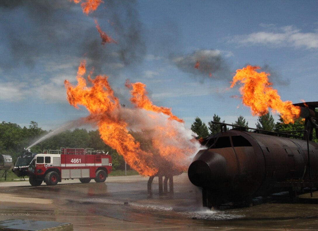 Propane-fueled flames rise from a burnt aircraft simulator recently.  The 932nd Airlift Wing Civil Engineering Squadron fire fighters, along with the wing commander, Col. Karl Goerke, drive a fire truck and spray water over the top of a live fire at the range on Scott Air Force Base.  The unit went through several drill with the simulated aircraft fire to be prepared for the real thing if it ever occurs in the future.  (U.S. Air Force photo/Maj. Stan Paregien)