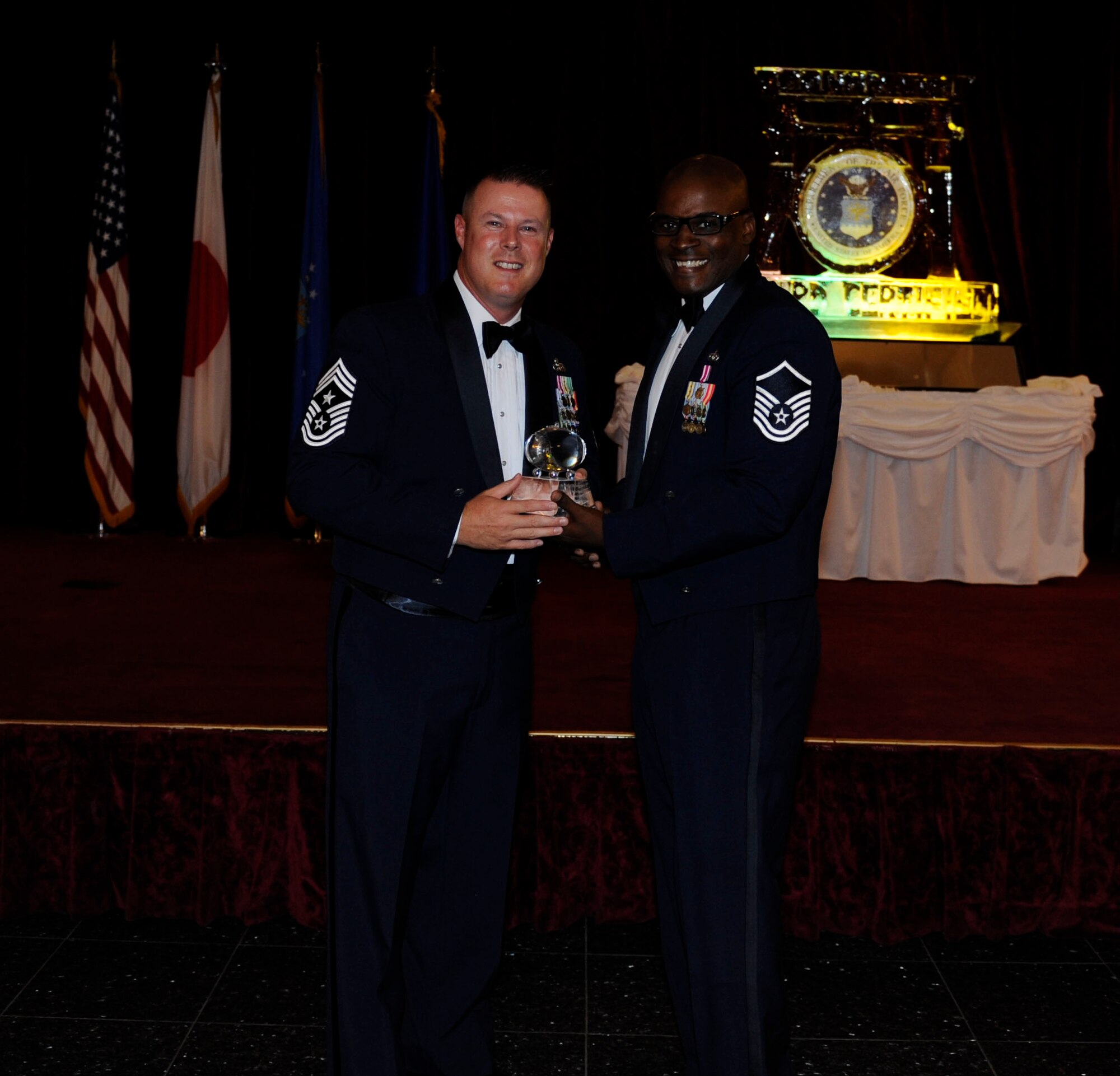 U.S. Air Force Master Sgt. Cedric Foster, the Top 3 president, presents a memento to Chief Master Sgt. Charles Hoffman, 18th Wing command chief master sergeant, during the Senior NCO induction ceremony Aug. 28, 2015, on Kadena Air Base, Japan. The memento commemorates the ceremony and shows appreciation to Chief Master Sgt. Hoffman for being the guest speaker. (U.S. Air Force photo by Airman 1st Class Lynette M. Rolen)