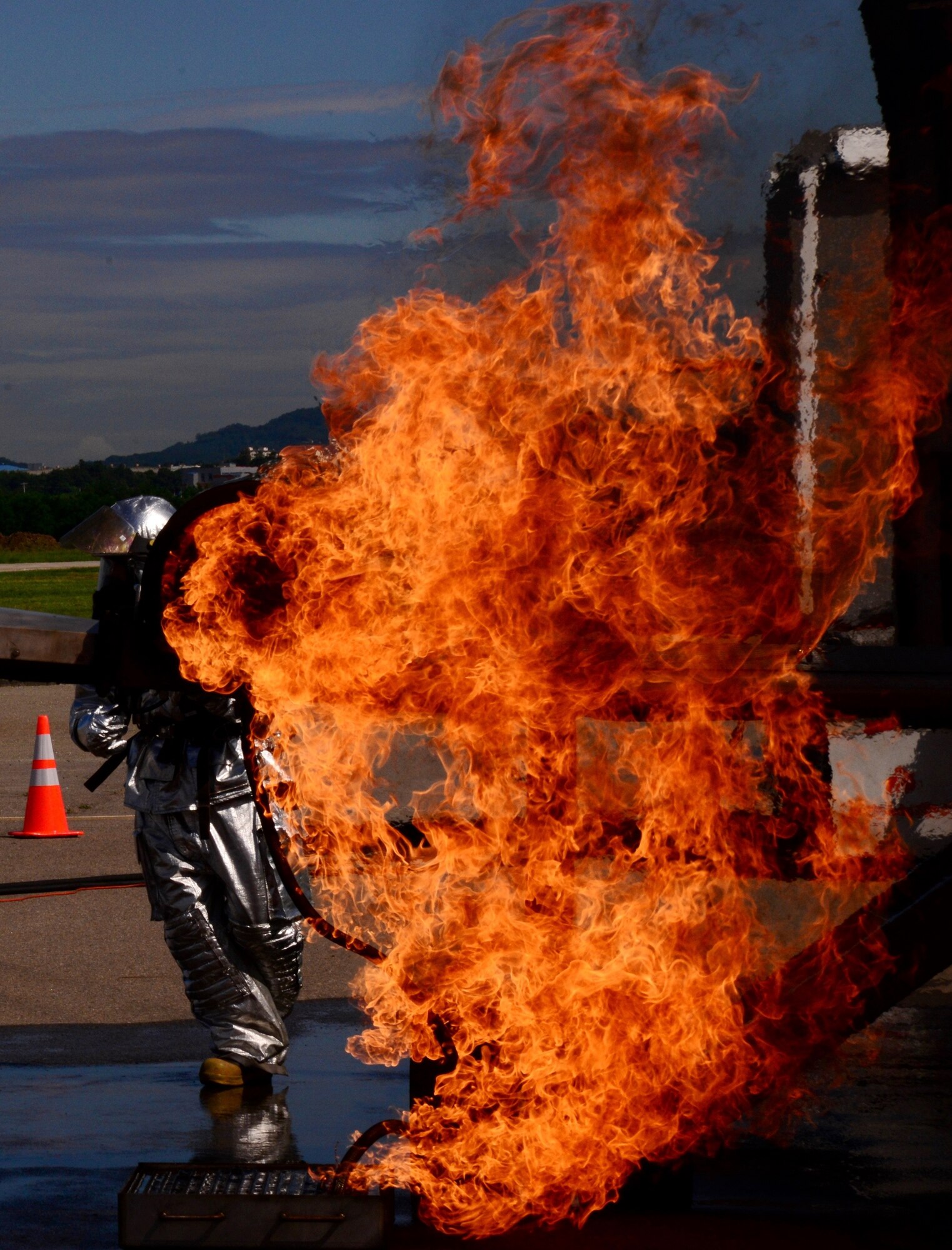 Staff Sgt. Michael White, 51st Civil Engineer Squadron crew chief, stands behind an aircraft fire during a training event Aug 26, 2015, at Osan Air Base, Republic of Korea. The outside areas of the practice aircraft are lit up to test how the firefighters handle extinguishing fires outside the simulated crashed aircraft, then inside the cockpit where pilots are and finally, inside the cargo area to try and save or recover any equipment. (U. S. Air Force photo by Staff Sgt. Benjamin Sutton) 