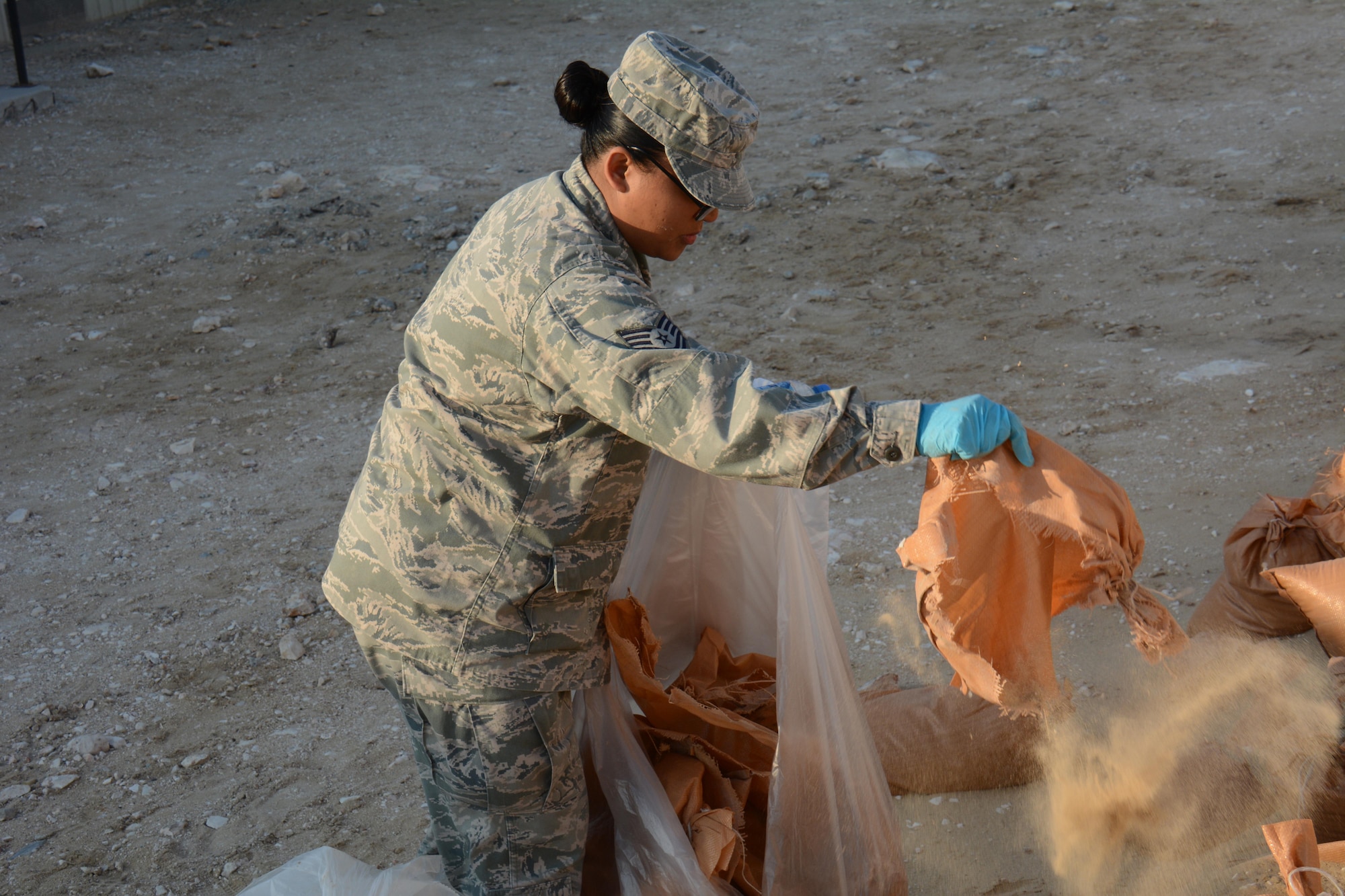 Tech. Sgt. Jocelyn Ferber, U.S. Air Force’s Central Command's Protocol non-commissioned officer in charge, shakes out sand from a broken sandbag during an Operation Community clean-up event at Al Udeid Air Base, Qatar Dec. 1. Ferber, a native of Joint Base Lewis-McChord, Washington, said she enjoyed helping clean up the base. More than 70 volunteers took part in the event collecting 130 bags of trash in one hour. (U.S. Air Force photo by Tech. Sgt. James Hodgman/Released)