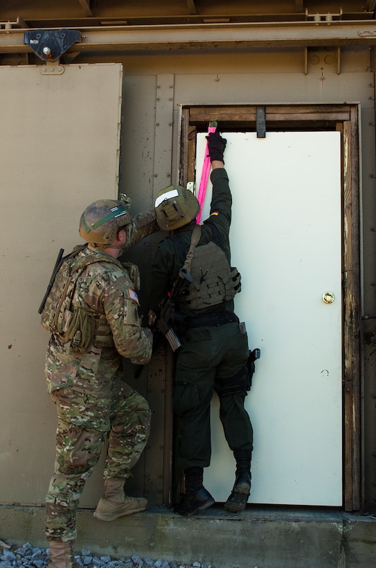 A U.S. Army Green Beret, left, coaches a member of the Colombian Compañía Jungla Antinarcóticos as he emplaces an explosive door-breaching charge on the entryway outside a shoot house during a joint training exercise on Eglin Air Force Base, Fla., Nov. 20, 2015. U.S. Army photo by Maj. Thomas Cieslak