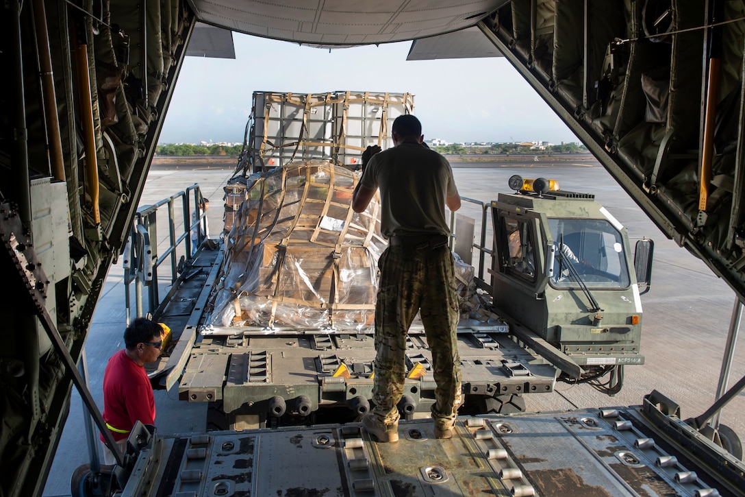 U.S. Air Force Senior Airman Zachary McGhee, center, directs a K-Loader behind a C-130J Super Hercules aircraft on Camp Lemonnier, Djibouti, Nov. 24, 2015. McGhee is a loadmaster assigned to the 75th Expeditionary Airlift Squadron. U.S. Air Force photo by Senior Airman Peter Thompson
