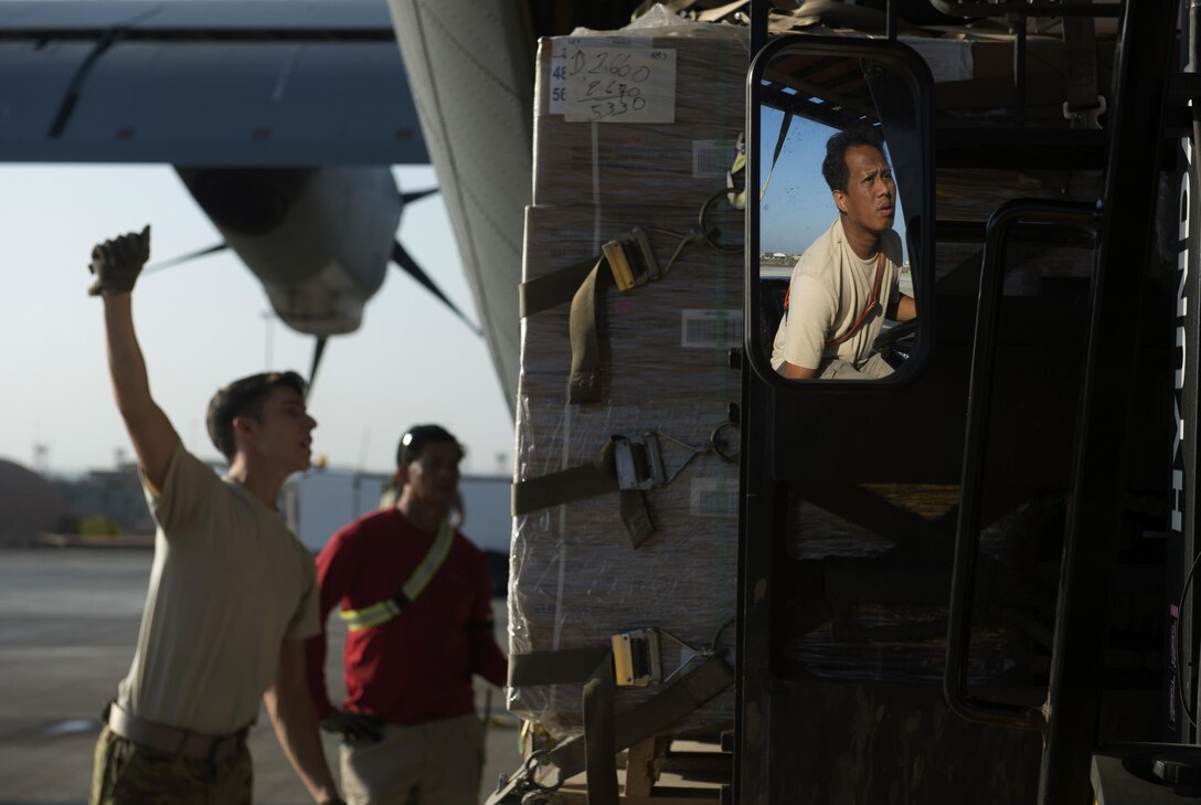 U.S. Air Force Senior Airman Zachary McGhee, left, uses hand signals to communicate directions with a forklift operator behind a C-130J Super Hercules aircraft on Camp Lemonnier, Djibouti, Nov. 24, 2015. McGhee is a loadmaster assigned to the 75th Expeditionary Airlift Squadron. U.S. Air Force photo by Senior Airman Peter Thompson