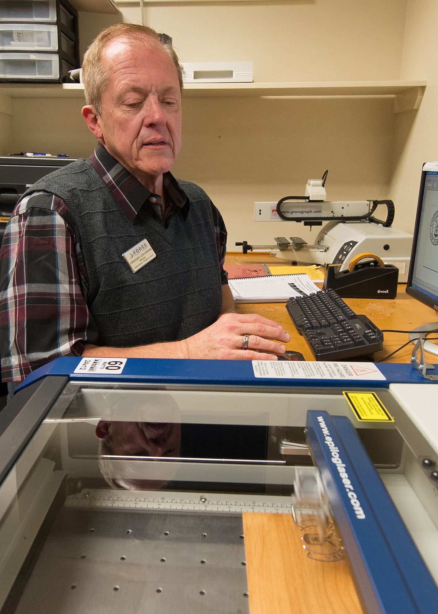 Gregory Leschishin, Tickets and Tours manager, watches as the Air Force logo is engraved on a piece of wood Dec. 1 at Outdoor Recreation in Building 1530. The engraving machine was recently purchased by the 66th Force Support Squadron to expand the engraving capabilities. (U.S. Air Force photo by Mark Herlihy)