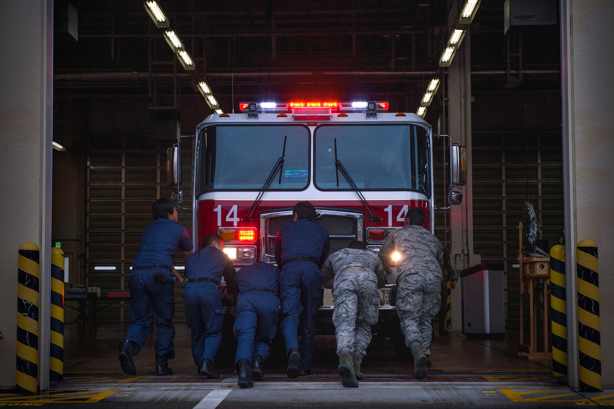 Firefighters with the 374th Civil Engineer Squadron firefighters push Fire Engine 14 into the main fire station at Yokota Air Base, Japan, Nov. 25, 2015. Yokota firefighters pushed the new engine into the apparatus bay by hand to conclude the blessing of the fleet ceremony for Fire Engine 14. (U.S. Air Force photo by Airman 1st Class Delano Scott/Released)