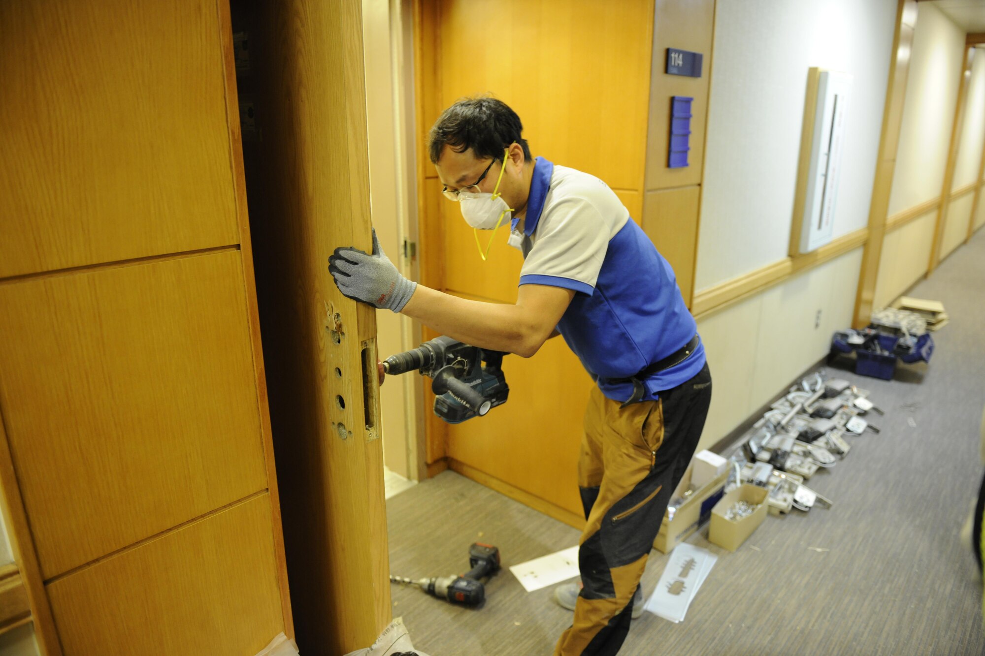 A Korean national contractor drills holes in a door to adjust for the new smart locks in building 535 at Kunsan Air Base, Republic of Korea, Dec. 2, 2015. The dormitory buildings are being changed to smart locks as part of a three phase program to reduce dormitory lockouts.