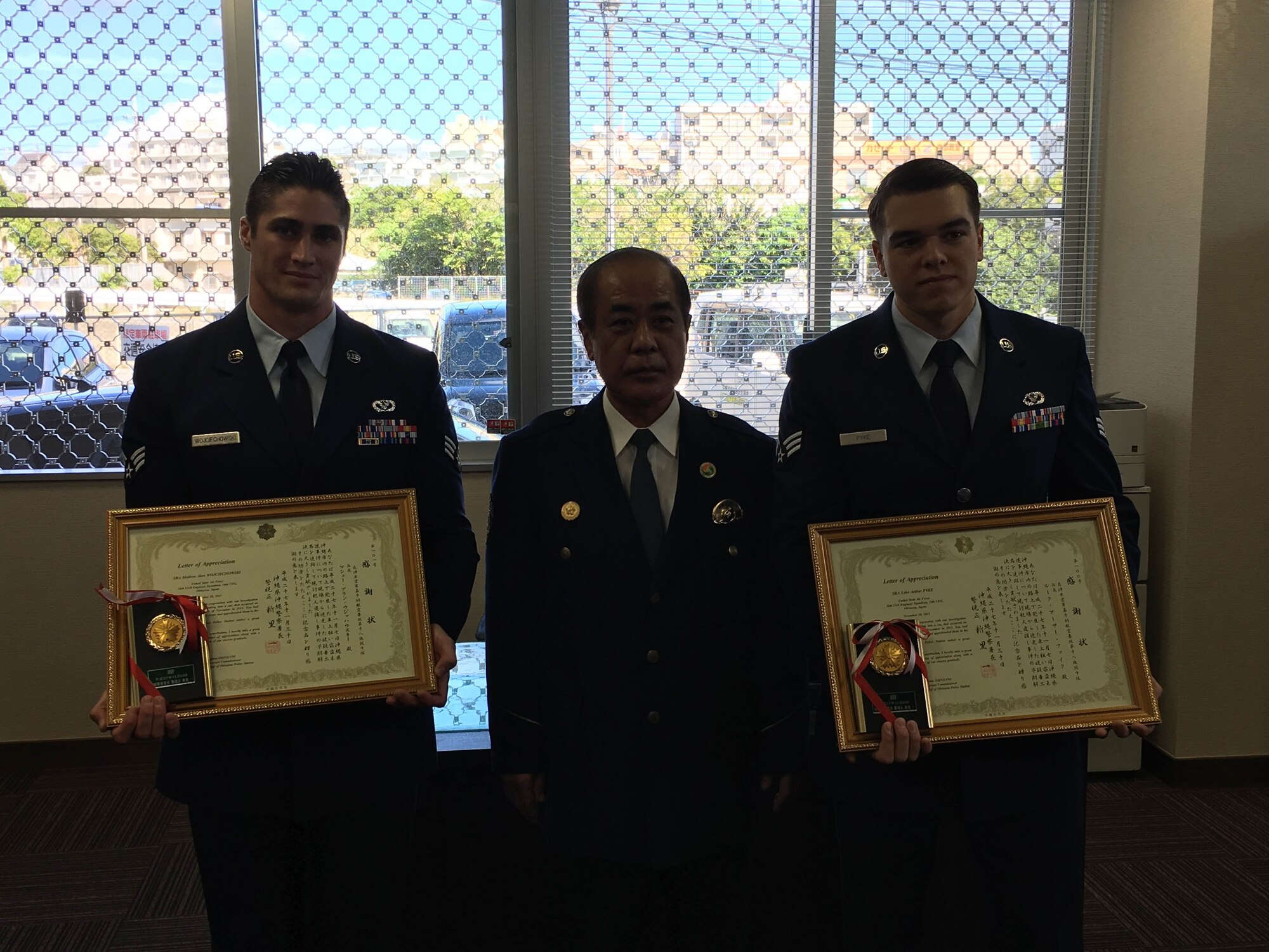 U.S. Air Force Senior Airmen Matthew Wojciechowski and Luke Fyke, 18th Civil Engineer Squadron electrical systems journeymen, receive certificates of appreciation from Hajime Shinzato, Okinawa Police Station chief, Nov. 30, 2015, at Okinawa Police Station, Okinawa, Japan. The Airmen played a vital role in preventing a crime by detaining two would-be robbers and waiting for police to arrive at the scene. (Courtesy photo)