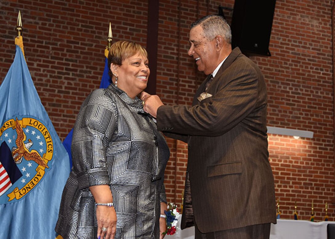 President of the American Federation of Government Employees Local 1992, Lucy Lewis receives her retirement pin from her brother, retired Navy Master Chief Petty Officer Thomas Keiser, during a ceremony Nov. 24, 2015 in the Frank B. Lotts Conference Center on the occasion of her retirement from federal service after 41 years. 