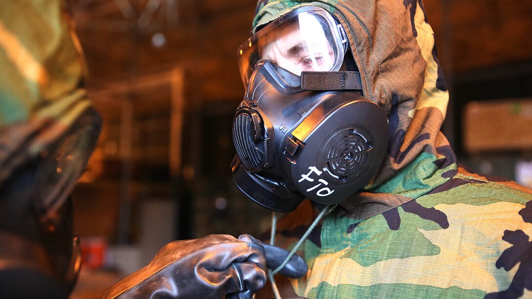 A reconnaissance, surveillance and decontamination Marine assists a peer to suit up mission-oriented protective postures four gear during a simulated chemical attack at the Marine Wing Support Squadron 171 motor transportation at Marine Corps Air Station Iwakuni, Japan, Nov. 18, 2015. As part of an operational decontamination exercise, this is just a glimpse of MWSS-171's annual unit level chemical, biological, radiological and nuclear defense training that enables combat proactivity and readiness.