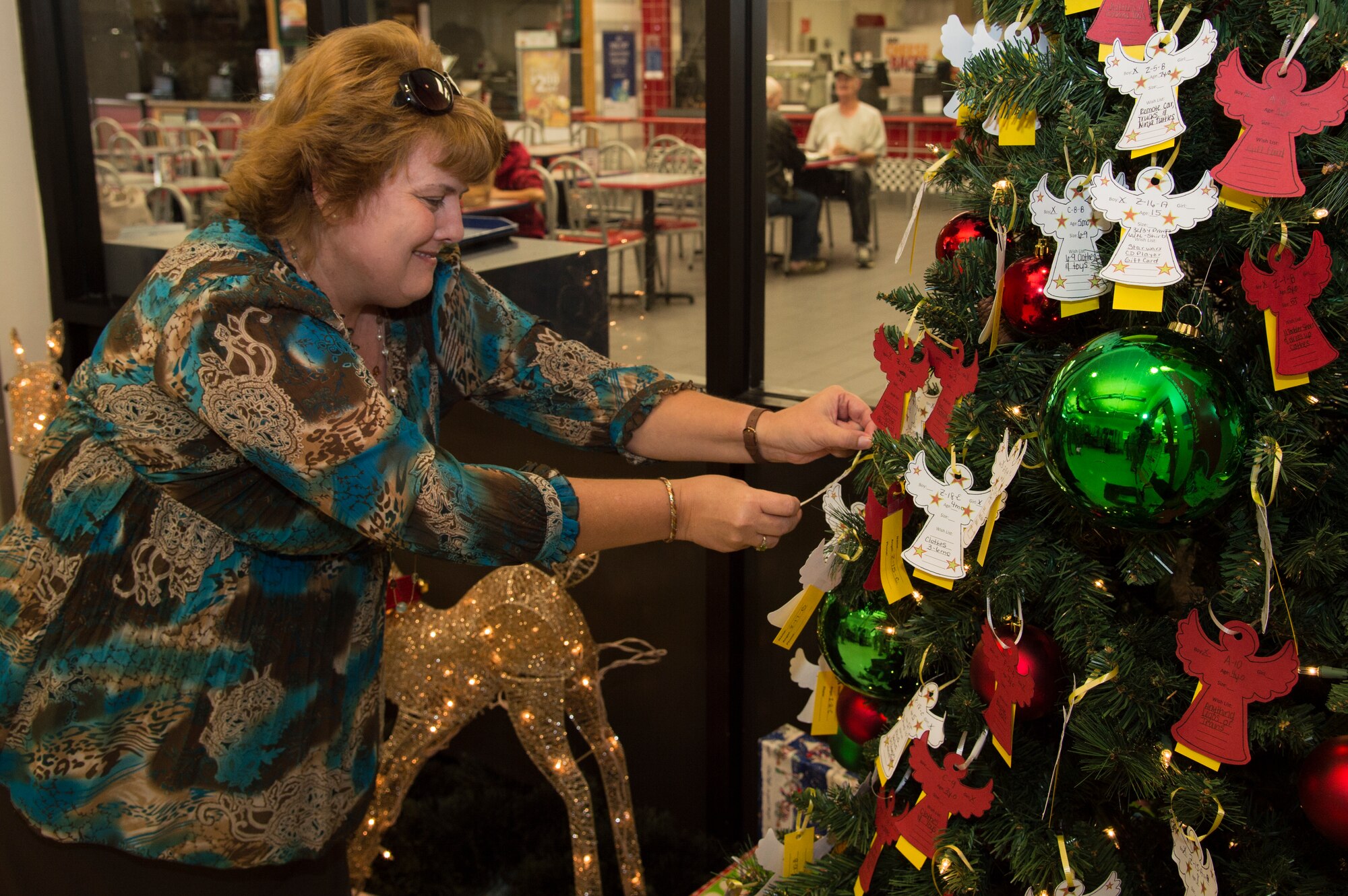 Karen White, Airman and Family Services Flight chief, plucks an ornament from the tree during the Angel Tree unveiling, Nov. 30, 2015, at Moody Air Force Base, Ga. The Angel Tree program is designed to improve the holiday season for military families by providing the children of Moody members with gifts. (U.S. Air Force photo by Staff Sgt. Eric Summers Jr./Released)