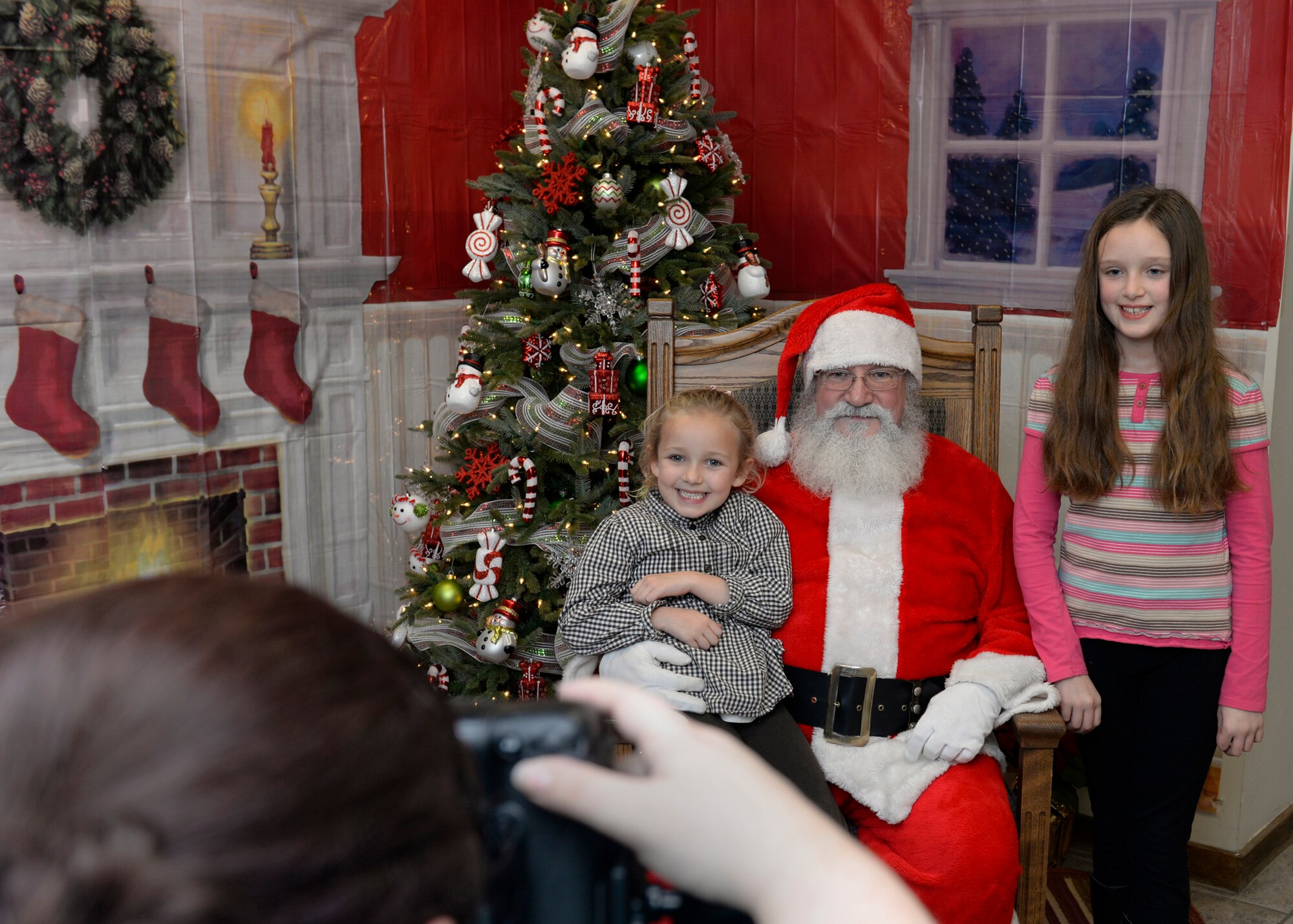 Sisters Emily and Isabella Goeke pose with Santa Claus for a photo during the annual tree lighting event in the chapel annex Dec. 2. Following the tree lighting ceremony outdoors, families were invited in the annex for crafts, cookies and photos with Santa. (U.S. Air Force photo by Mark Wyatt)